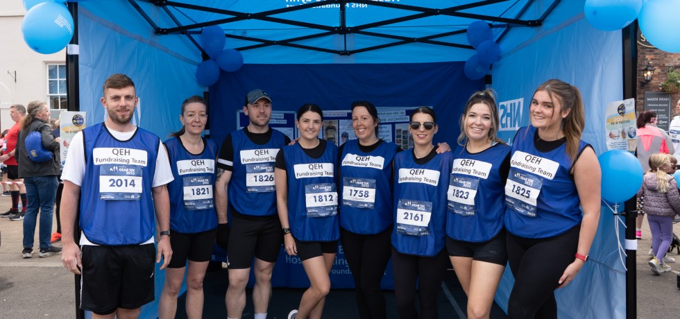 From left to right Jake Kenyon, Emma Southwell, Ryan Oakes, Hannah Auker, Lorraine Hunt, Fay Collison, Hollie Nelson and Ruby Kirby are standing in front of the Queen Elizabeth Hospital gazebo, smiling before the 2023 GEAR 10K race.