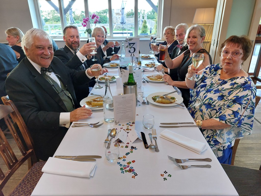 A picture of Freemasons members and families gathered around a table, holding up wine glasses in celebration.