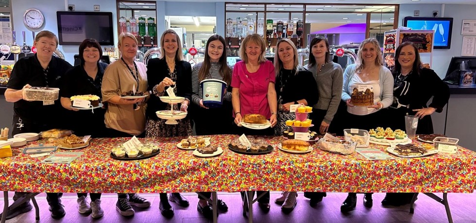 A picture of many bakers holding their plates and donation bucket during their coffee morning