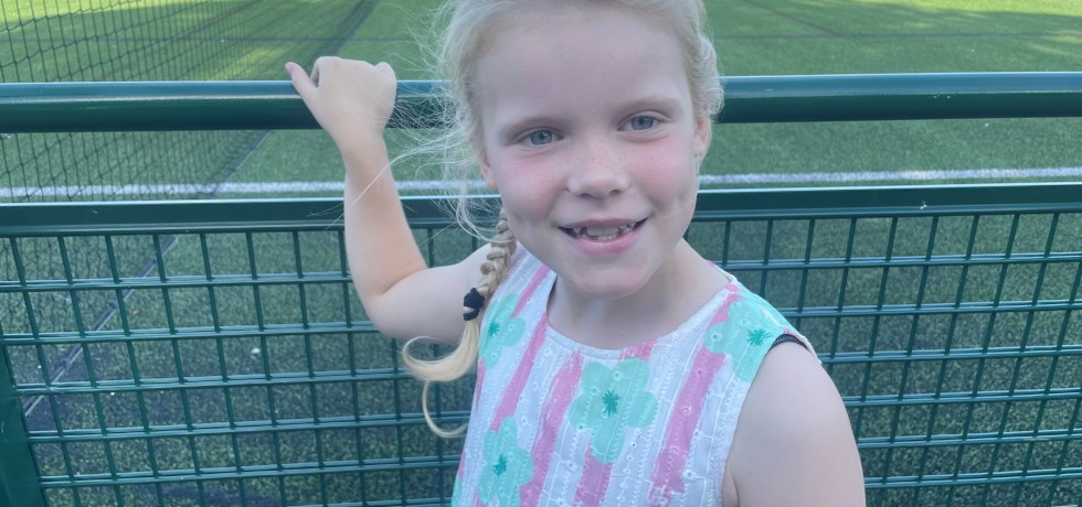 Little girl standing in front of a football pitch smiling.
