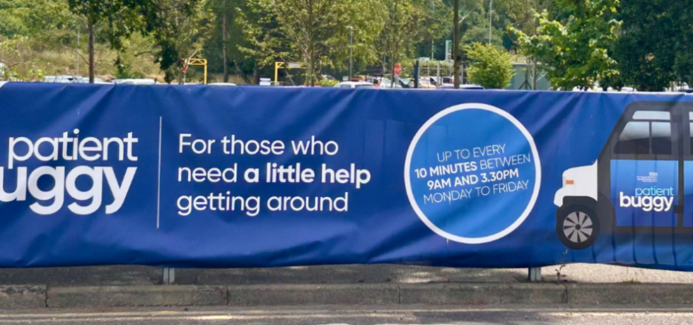 A landscape photo of a fabric banner on railing outside the hospital. The banner depicts the patient buggy. It reads "Free patient buggy. For those who need a little help getting around. Up to every 10 minutes between 9am and 3.30pm Monday to Friday"