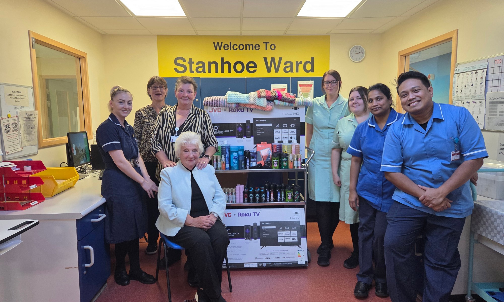 A photo of staff nurses with two flat screen television sets and lots of body wash, deodorants, etc. The mother and daughter duo can be found on the far right with Val sat in a chair.