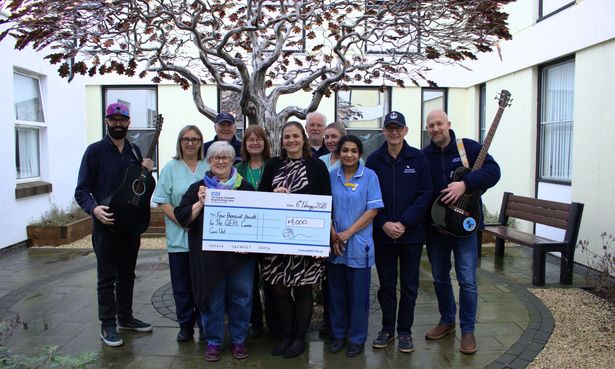 Nelson’s Shanty Men holding guitars and a giant novelty cheque with nursing staff around