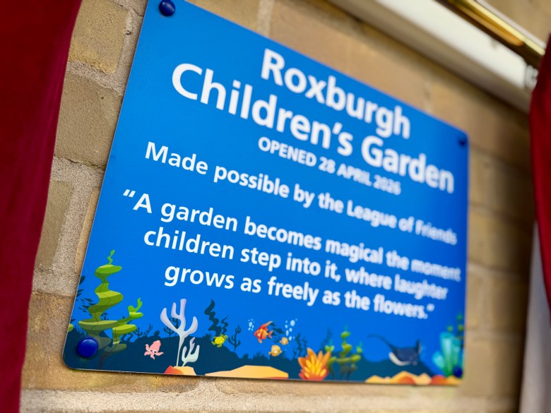 An aquatic-themed plaque on a brick wall which reads "Roxburgh Children's Garden. Opened 28 April 2026. Made possible by the League of Friends. "A garden becomes magical the moment children step into it, where laughter grows as freely as the flowers."