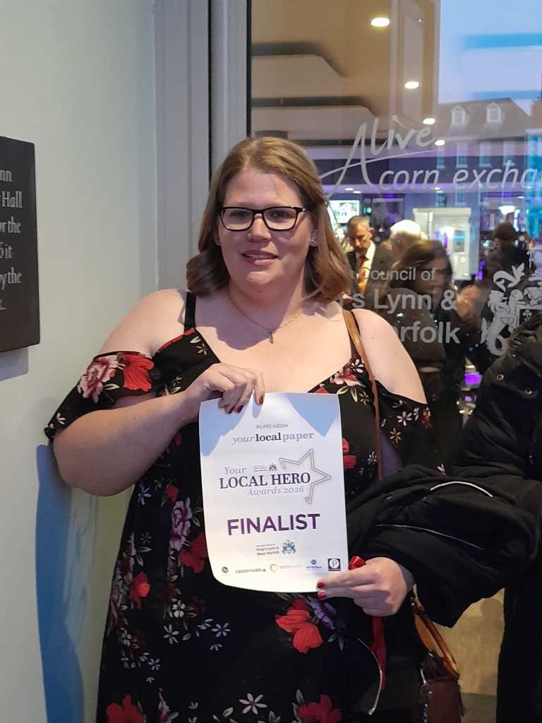 Maggie Drew in a stunning black and red dress holding up a "Your Local Hero Awards 2026 Finalist" certificate.