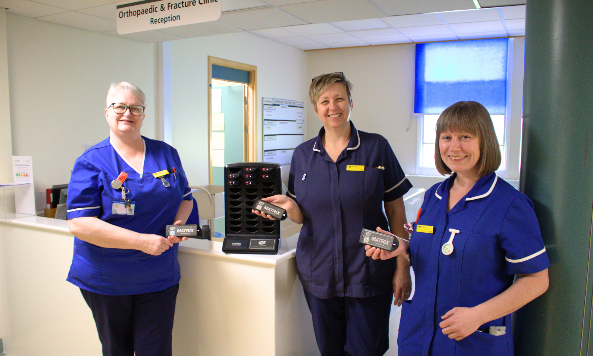 A photo of some nurses holding a small pager next to the pager charging tower
