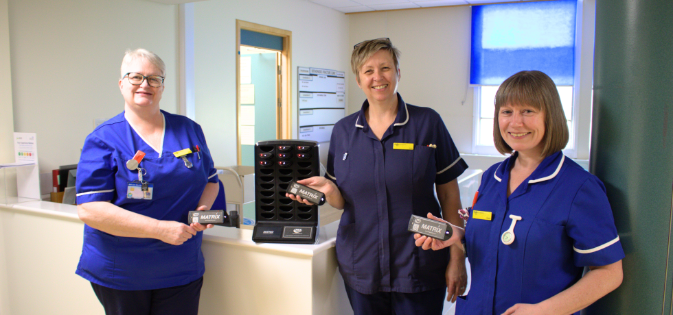 A photo of some nurses holding a small pager next to the pager charging tower
