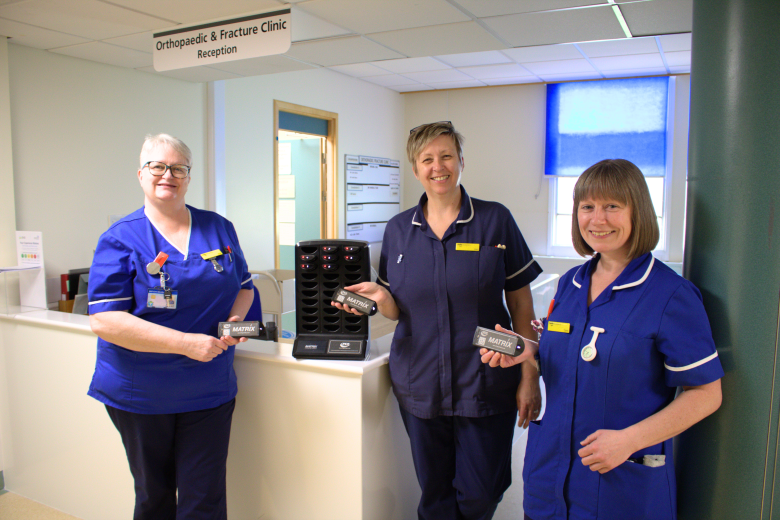 A photo of some nurses holding a small pager next to the pager charging tower