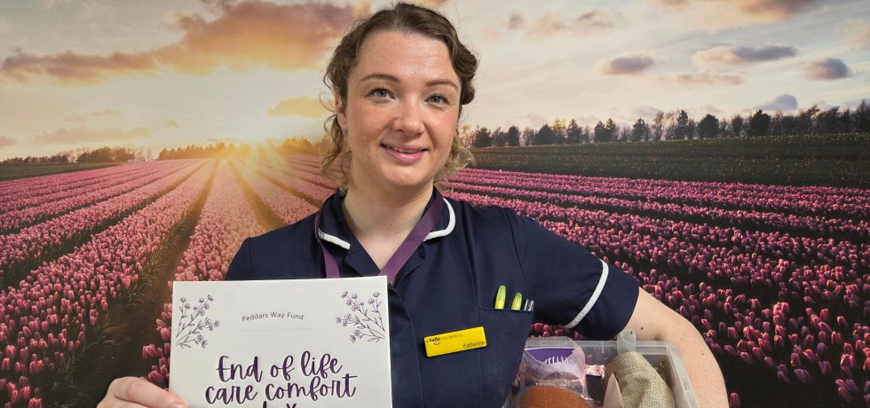 A nurse with blond hair holding a box and a poster in front of a purple background