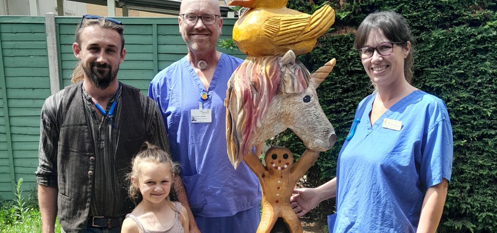 A photo of two nurses stood next to Billy Bicknell and Jeana next to a large totem pole consisting of a capybara, a penguin, a gingerbread man, a unicorn and a duck.