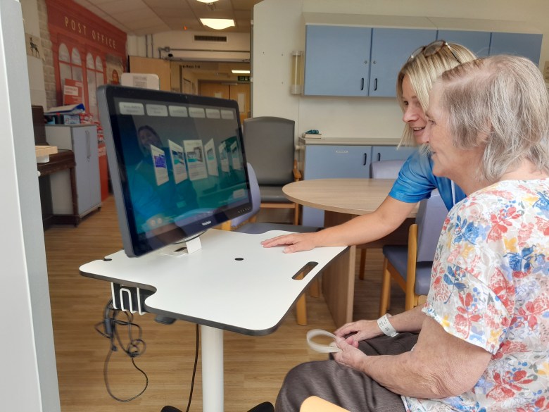 A photo of a dementia specialist nurse introducing a smiling patient to the computer system, RITA