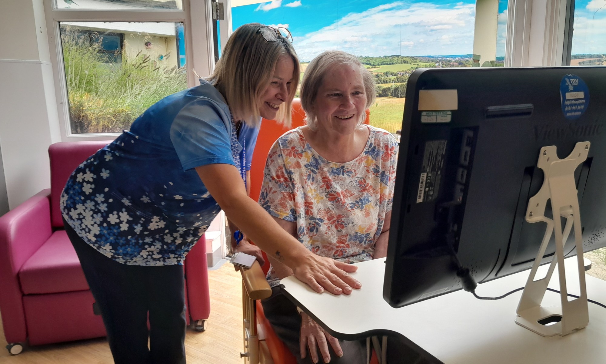 A photo of a dementia specialist nurse introducing a smiling patient to the computer system, RITA