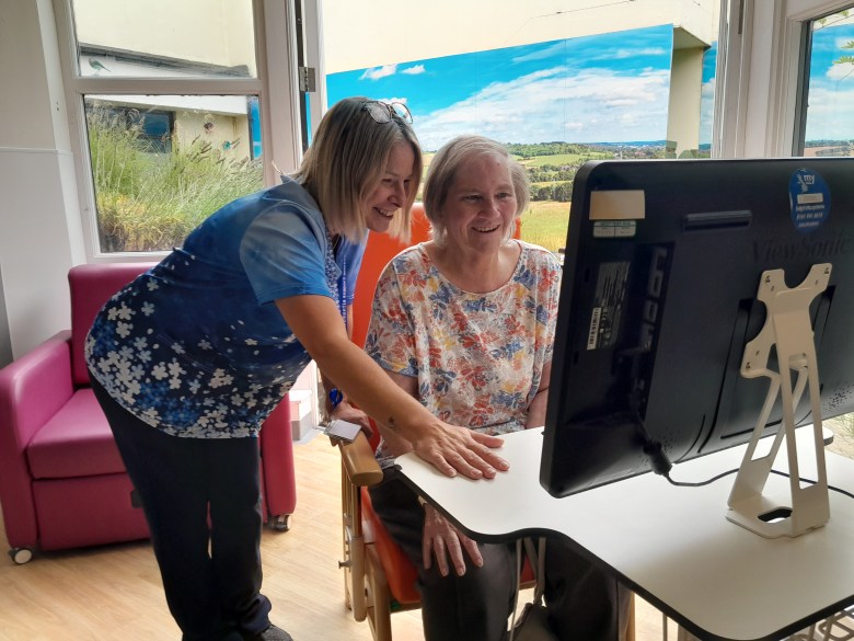 A photo of a dementia specialist nurse introducing a smiling patient to the computer system, RITA