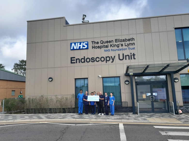 A photo of Brian Moss and his wife, Dianne, with a giant novelty cheque stood outside The Queen Elizabeth Hospital King's Lynn NHS Foundation Trust Endoscopy Unit.