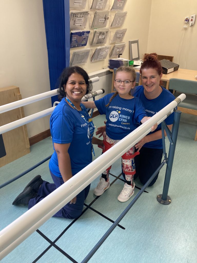A photo of physiotherapists helping to support a young patient during their therapy sessions. They are all wearing "I'm raising money for QEHKL Charity" t shirts